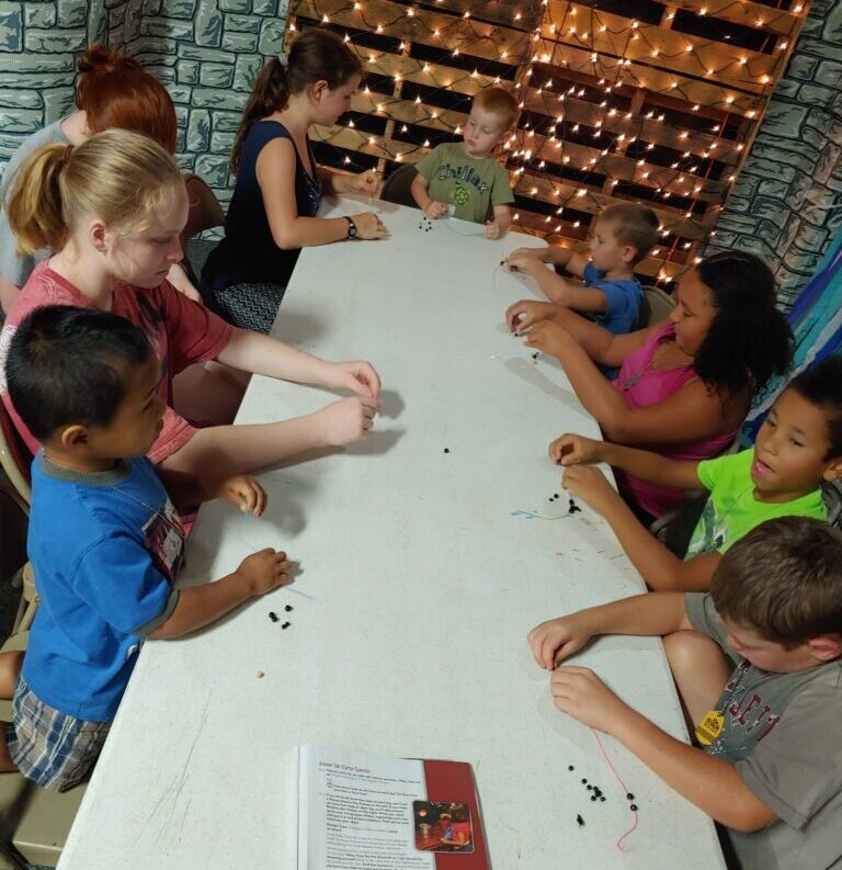 Kids beading a bracelet at a table.