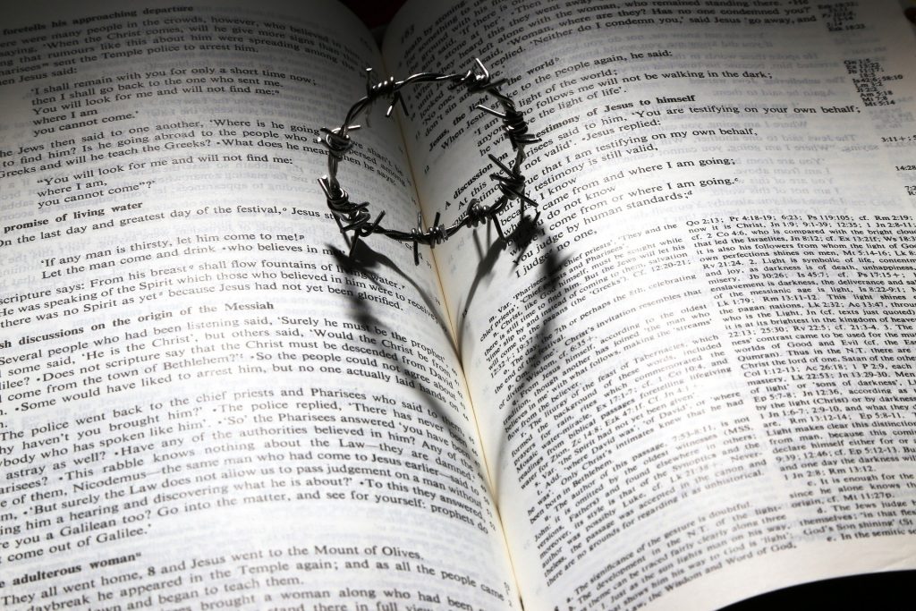 Open bible with a crown of thorns in the center. The shadow of the crown makes a heart on the book.